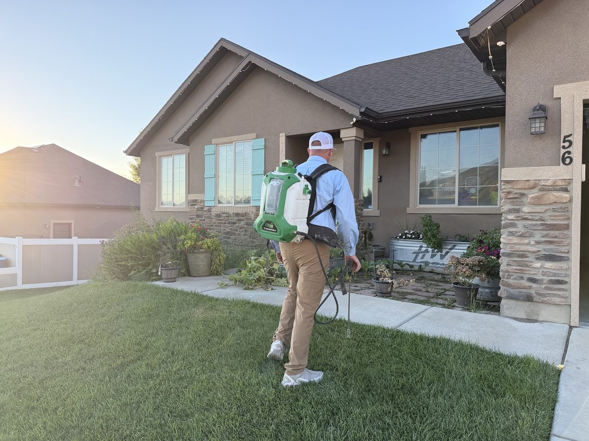 Technician treating the foundation and landscaping around a home at sunset